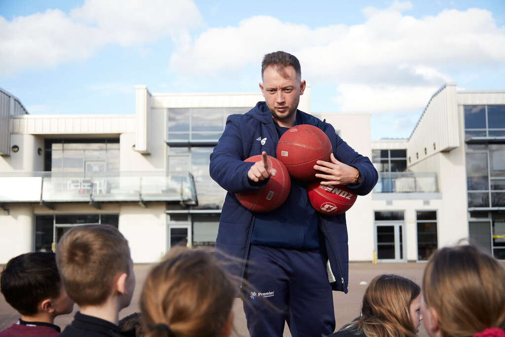 Premier Education coach holding 3 basketballs getting ready to teach children how to play basketball 