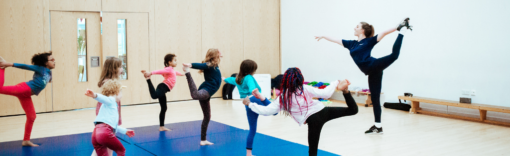 Premier Education coach teaching children to do gymnastics in a school PE session.