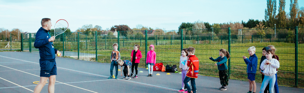 A Premier Education coach teaching children how to play tennis.